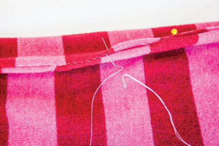 needle and thread sewing red and pink fabric with a whip stitch